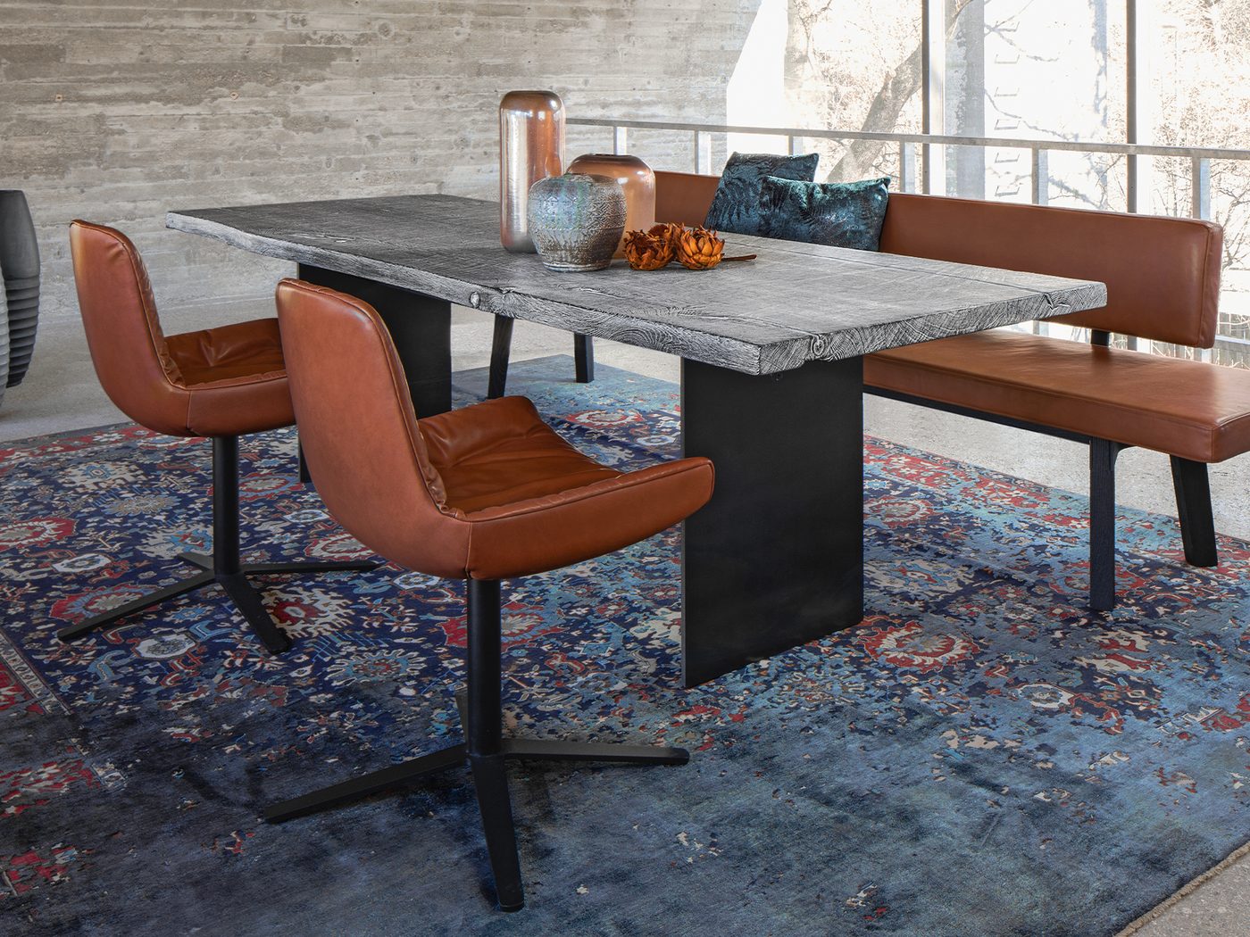 Janua-Esstisch aus geköhlter Eiche in Ton Grau mit Freifrau Leya Armchairs in Cognac-Leder und einer Sitzbank vor einer Betonwand